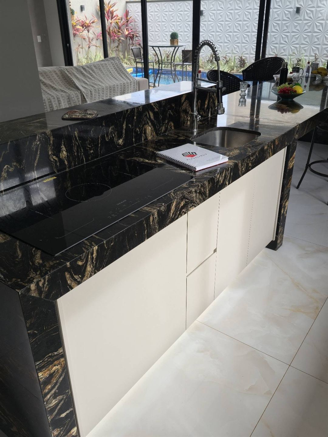 Ilha de cozinha com tampo de granito preto e dourado, frentes off-white e luz embutida embaixo